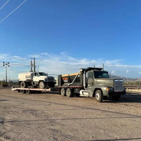 Phoenician Excavation Company dump truck and lowboy trailer hauling a water truck to a job site